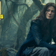 Moiraine, in a travel-worn blue dress, sits forlornly in a mossy forest.